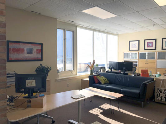 A view of the Dairy Dynamics office with sofa, cabinets, pictures and decorative prints of cows, desks, and computers. Big windows spill daylight onto the scene.